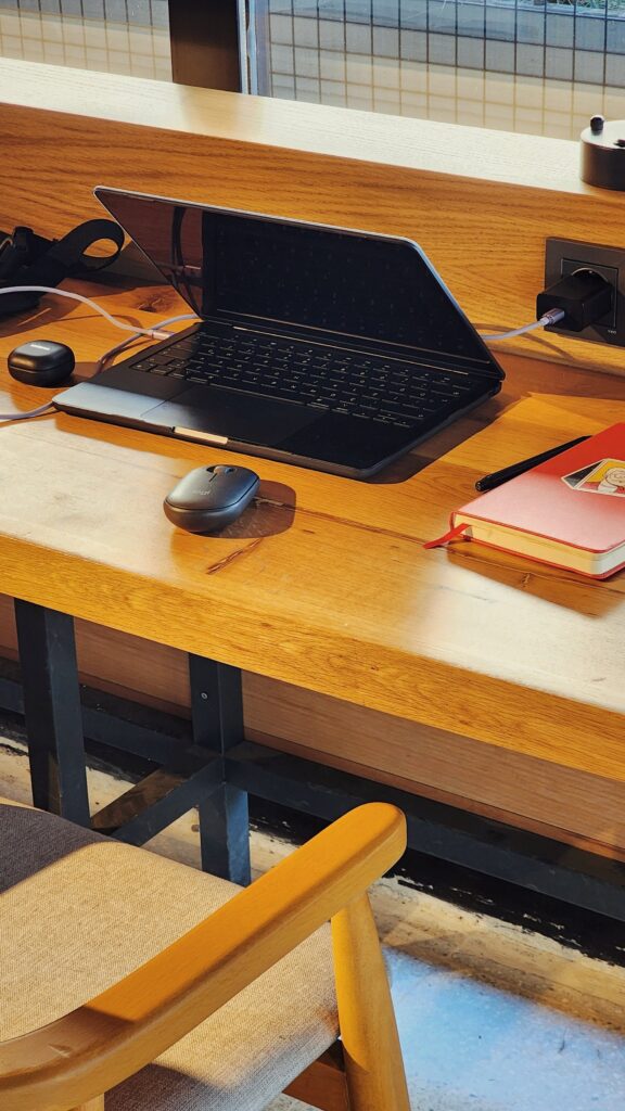 A laptop sits on a wooden desk with a mouse and a book